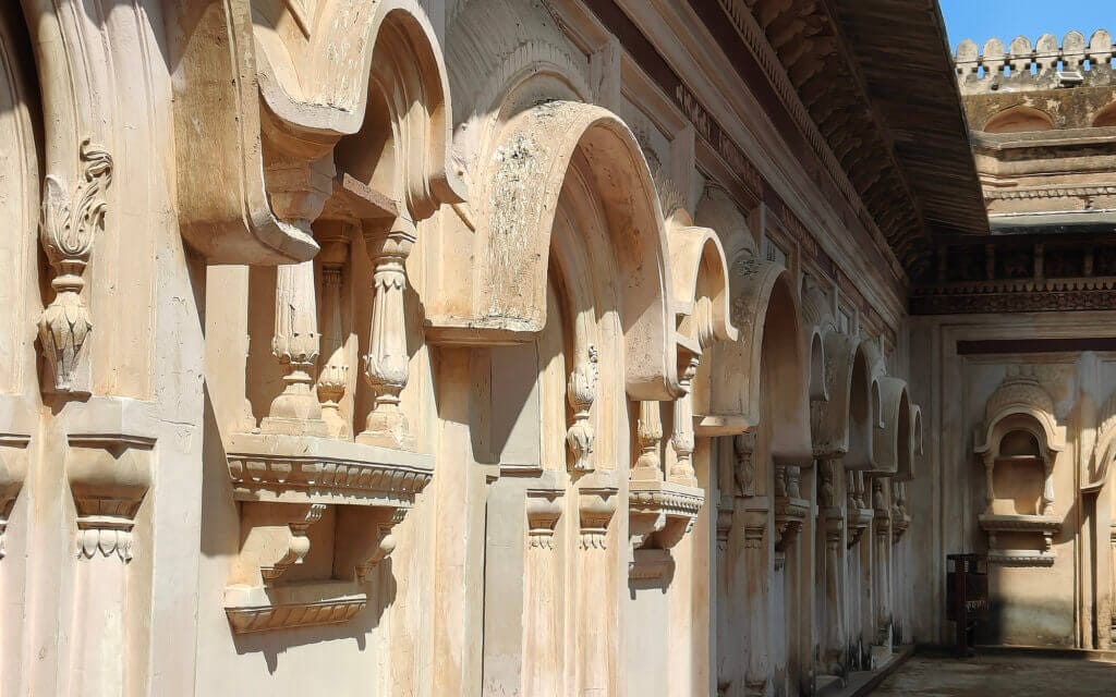 A row of ornate, arched windows with detailed carvings on a weathered, pale stone building, under a clear blue sky.